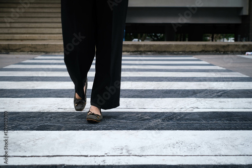 Person crossing a city street using a zebra crossing, emphasizing urban lifestyle and pedestrian safety. Legs and shoes visible, pavement background. photo