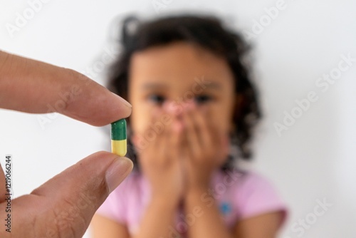 A mother's hand holding a pill capsule with a little girl covering her mouth with both hands. The concept of children refusing to take medicine. photo