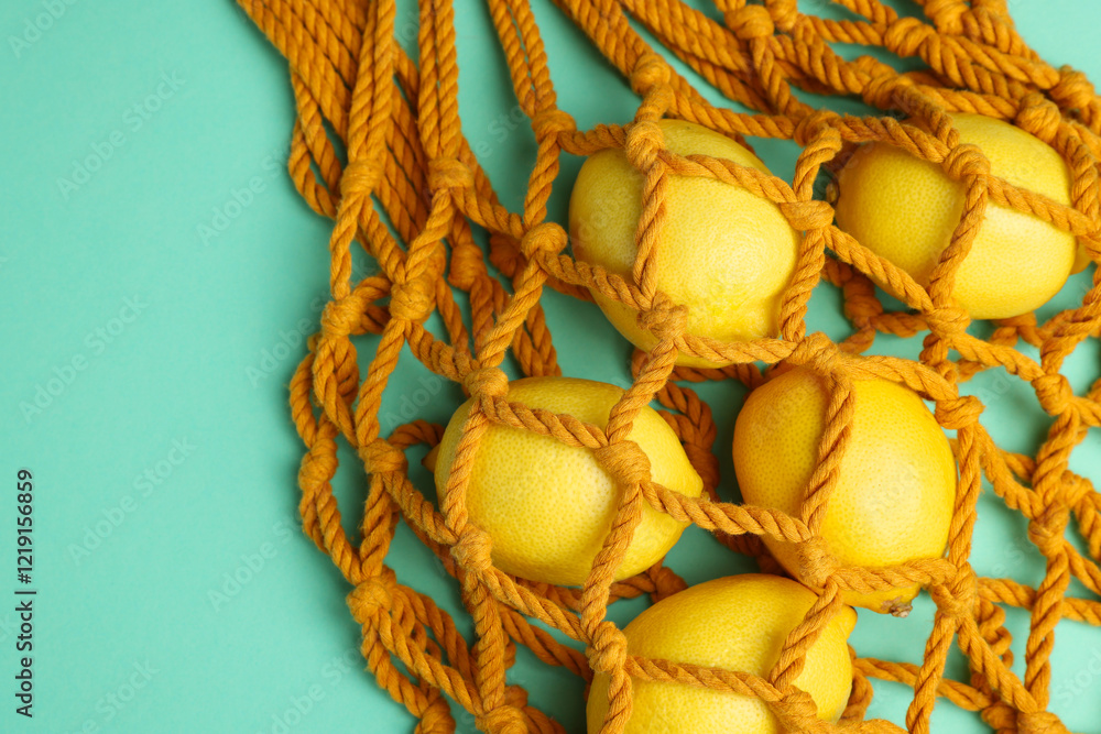 Naklejka premium Macrame shopping bag with lemons on turquoise background, top view. Space for text