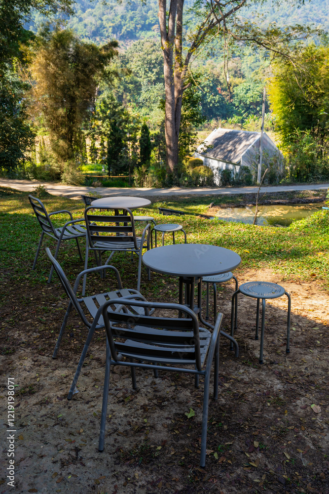 Fototapeta premium A serene outdoor seating area with metal chairs and tables surrounded by greenery and mountains in the background.