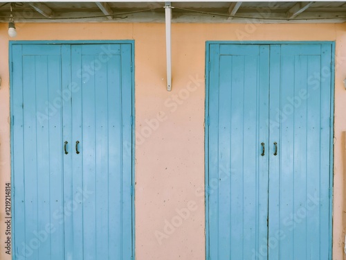 A pair of blue wooden doors against a peach-colored wall, showcasing simple architectural design and a calm aesthetic.