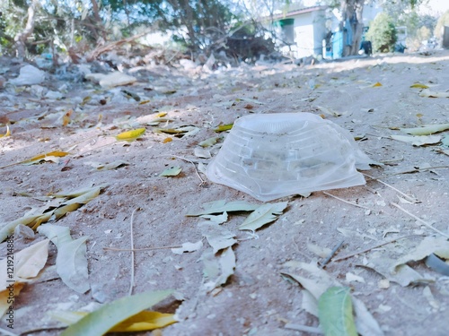 A discarded item lies on a dusty ground littered with leaves, surrounded by a natural setting.