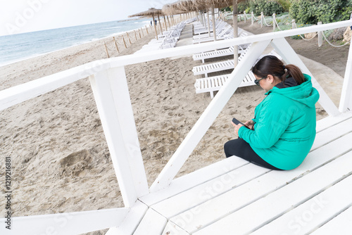 chica revisando su telefono movil mientras disfruta de la playa en primavera photo