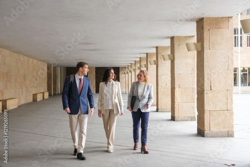 Three businesspeople are walking and talking in the hallway of a modern building