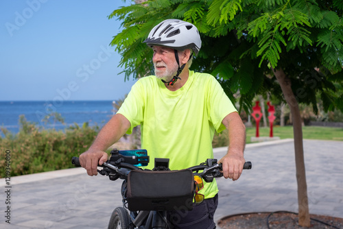 Senior athletic man with electric bicycle in outdoors excursion at sea wearing helmet enjoying freedom, authentic healthy retirement lifestyle #1219340800