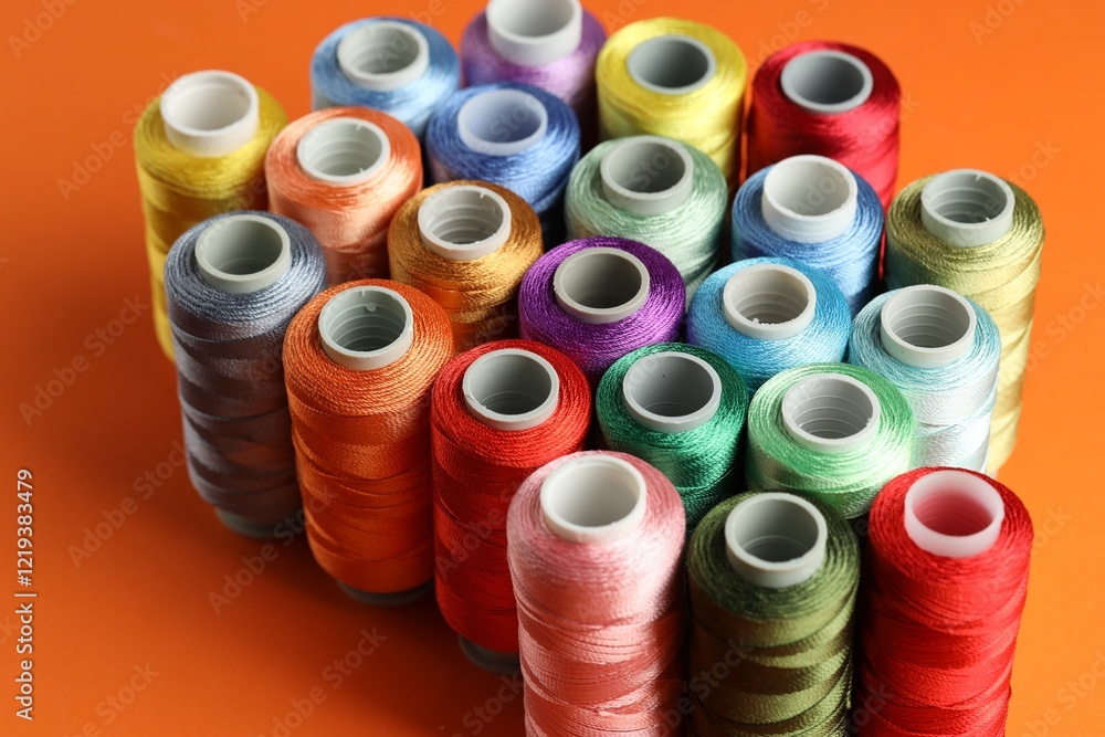 Different spools of sewing threads on orange background, closeup Different spools of sewing threads on orange background, closeup
