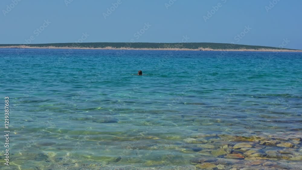 Man is swimming in the sea, and child is playing on the shore, splashing water with a toy scoop under the warm sun by the clear blue sea. The concept of children's joy, sea fun and summer vacation. Man is swimming in the sea, and child is playing on the shore, splashing water with a toy scoop under the warm sun by the clear blue sea. The concept of children's joy, sea fun and summer vacation.