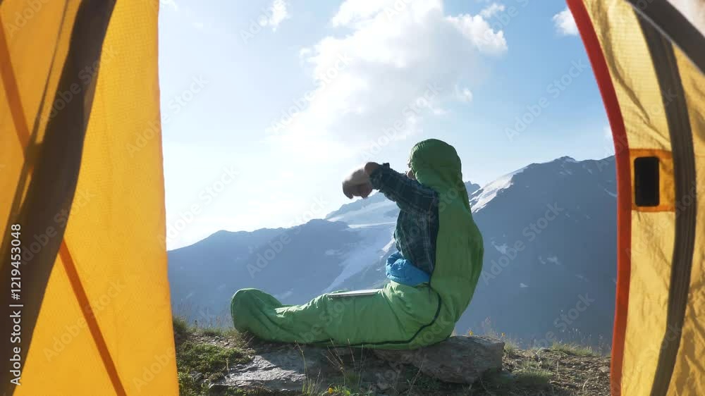 Digital nomad freelancer finishes working on laptop while sitting in sleeping bag at campsite in mountains and celebrates success with arms raised