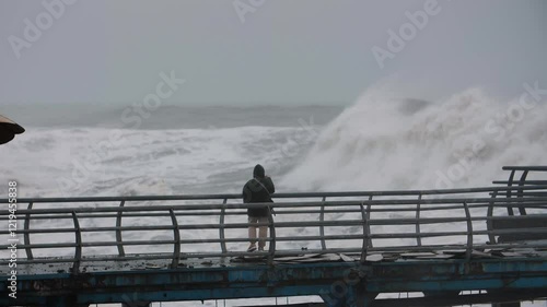 A man on the pier films very large waves on his phone