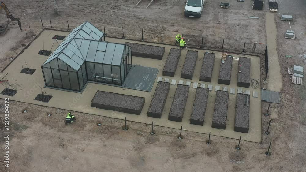 Workers installing a new fence near a greenhouse and garden beds in a foggy construction site landscape. Drone shot. Workers installing a new fence near a greenhouse and garden beds in a foggy construction site landscape. Drone shot.