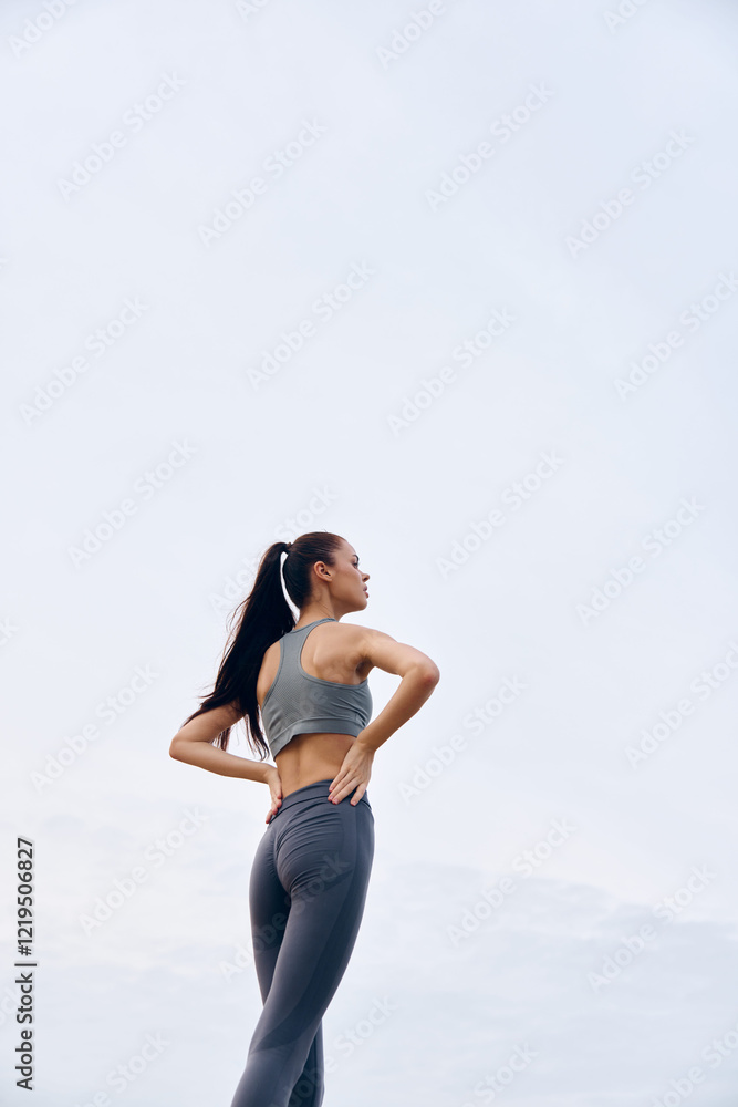Athletic woman in gray activewear enjoying workout outdoors, demonstrating strong posture and determination in a bright sky environment during warm weather Athletic woman in gray activewear enjoying workout outdoors, demonstrating strong posture and determination in a bright sky environment during warm weather