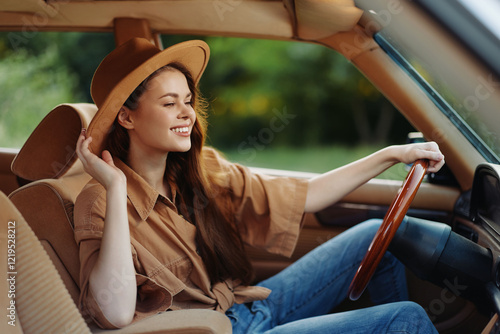 Fotografie Happy woman in a stylish outfit driving a vintage car, enjoying the sunny day with a playful smile, surrounded by nature in warm tones