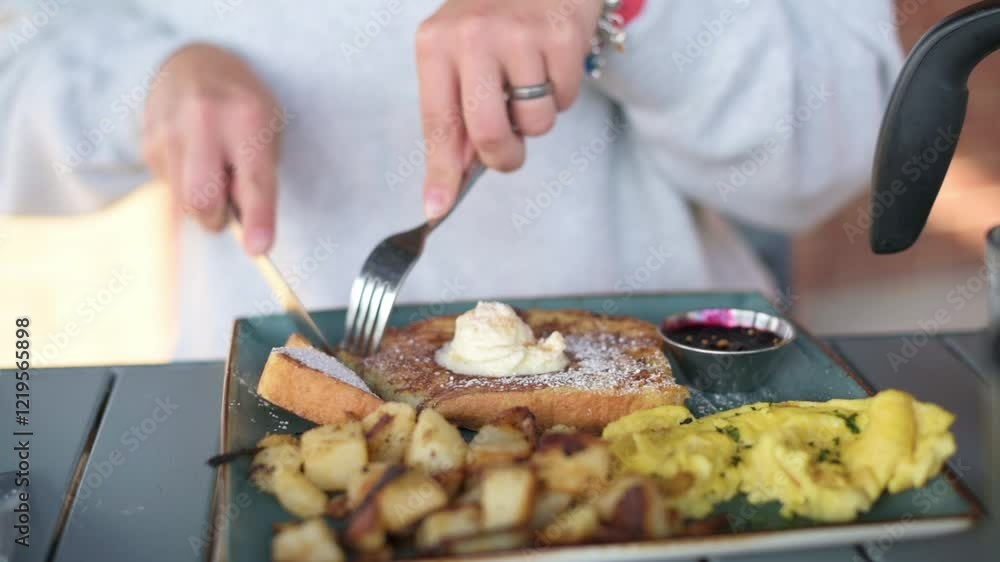 Enjoying a Hearty Breakfast with French Toast Sides person cutting into French toast topped with whipped cream, served with scrambled eggs, roasted potatoes, jam cozy breakfast setting French toast Enjoying a Hearty Breakfast with French Toast Sides person cutting into French toast topped with whipped cream, served with scrambled eggs, roasted potatoes, jam cozy breakfast setting French toast