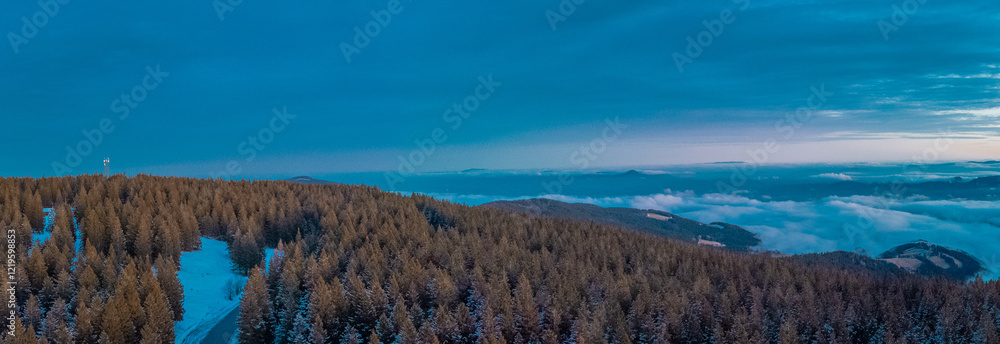 Epic drone panorama of Rogla ski resort in Pohorje region of Slovenia. Visible colorful sunset, clouds in the valley and small hills piercing through the clouds.