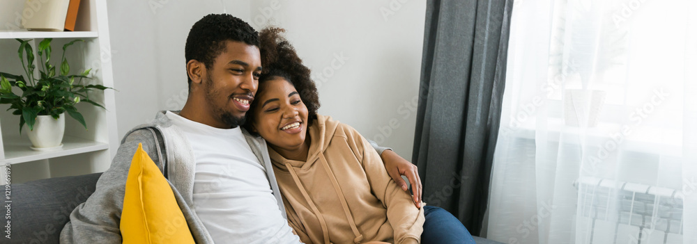 Banner copy space Happy African American couple enjoys quality time together while watching television. Man and woman seated closely on the couch, showcasing comfort and connection in a cozy home Banner copy space Happy African American couple enjoys quality time together while watching television. Man and woman seated closely on the couch, showcasing comfort and connection in a cozy home