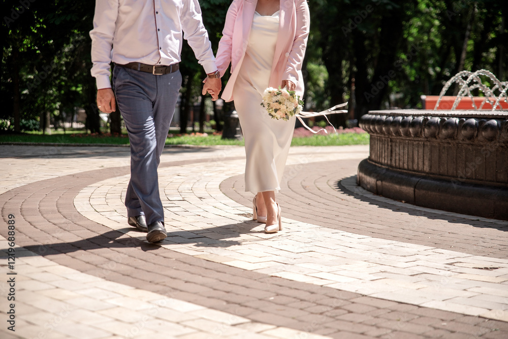 Obraz premium A bride in a white dress walking hand in hand with a groom near a fountain