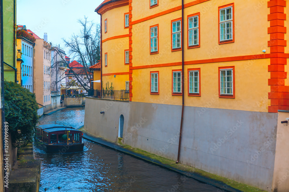 Picturesque scene of Certovka canal in Prague, with a boat navigating narrow waterway flanked by colorful buildings. Vibrant building along with serene water and boat create a charming atmosphere