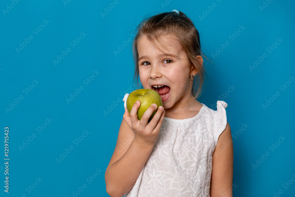 Cute child smiling bites apple. nutrition for caries prevention. portrait of little girl with fruit on blue background. kid eating healthy food, snack. teeth, dental health, smile. children dentistry Cute child smiling bites apple. nutrition for caries prevention. portrait of little girl with fruit on blue background. kid eating healthy food, snack. teeth, dental health, smile. children dentistry