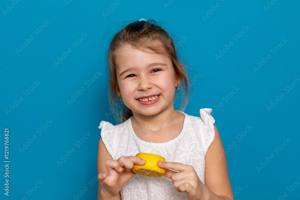 Funny little child girl try to taste fresh lemon, wrinkles and makes a grimace. Sour taste, facial emotions negative, in white dress, isolated blue background, copy space. High quality photo Funny little child girl try to taste fresh lemon, wrinkles and makes a grimace. Sour taste, facial emotions negative, in white dress, isolated blue background, copy space. High quality photo