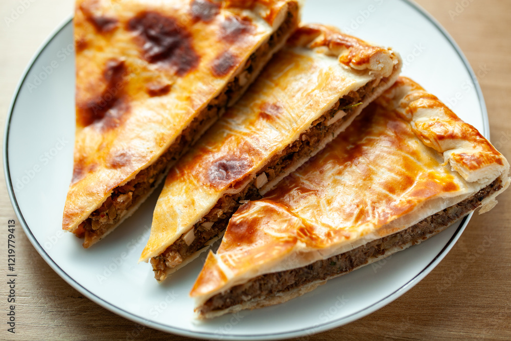 Three slices of traditional Russian meat pies served on a white plate The pies have a golden brown crust and are filled with minced meat Three slices of traditional Russian meat pies served on a white plate The pies have a golden brown crust and are filled with minced meat