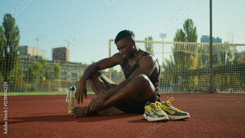 African American footballer sportsman sit on field suffer pain sharp ache muscle cramp foot injury sporty man injuring leg in training outside sport trauma damage feet painful joint workout outdoors
