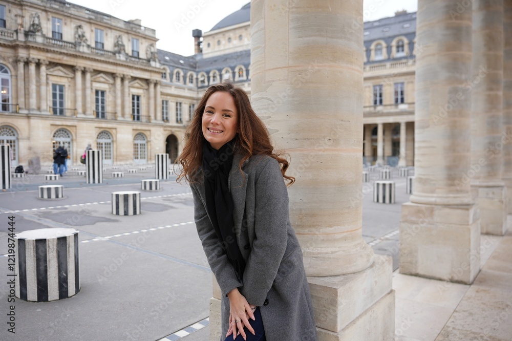 A cheerful woman poses by a column in the courtyard of Palais Royal, Paris, surrounded by modern black-and-white art installations and historic French architecture. A cheerful woman poses by a column in the courtyard of Palais Royal, Paris, surrounded by modern black-and-white art installations and historic French architecture.