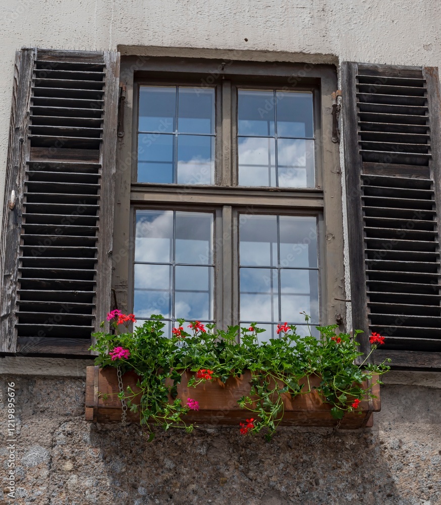 Wooden window with shutters with blooming flowers in pots in the wall of an old house Wooden window with shutters with blooming flowers in pots in the wall of an old house