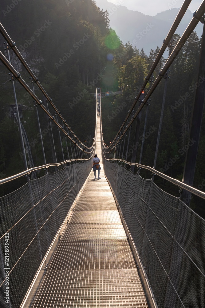 Obraz premium A modern metal suspension bridge over a mountain road in the Alps between two mountain peaks near Innsbruck. Highline179