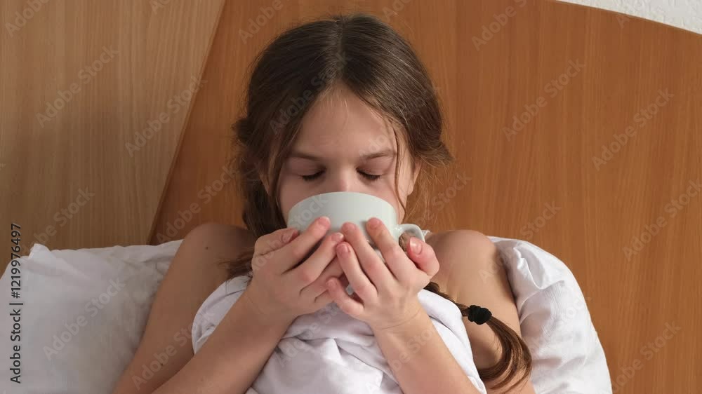 Sick little girl drinking hot tea to treat cough and sore throat, sitting on bed at home, close up. Drink for treatment of illness, flu and cold Sick little girl drinking hot tea to treat cough and sore throat, sitting on bed at home, close up. Drink for treatment of illness, flu and cold