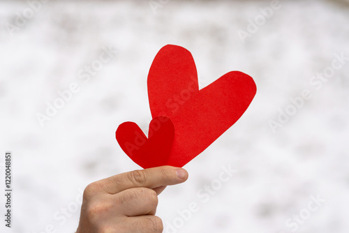 A cheerful man is showing two red paper hearts, one larger and one smaller, with a warm smile in a cozy indoor setting. Romantic gesture. Happy Valentine's Day. photo