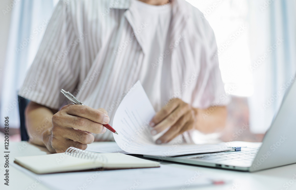 Fototapeta premium Asian man in casual clothes sitting at desk and using laptop working at home, freelancer working online and doing part time job at home