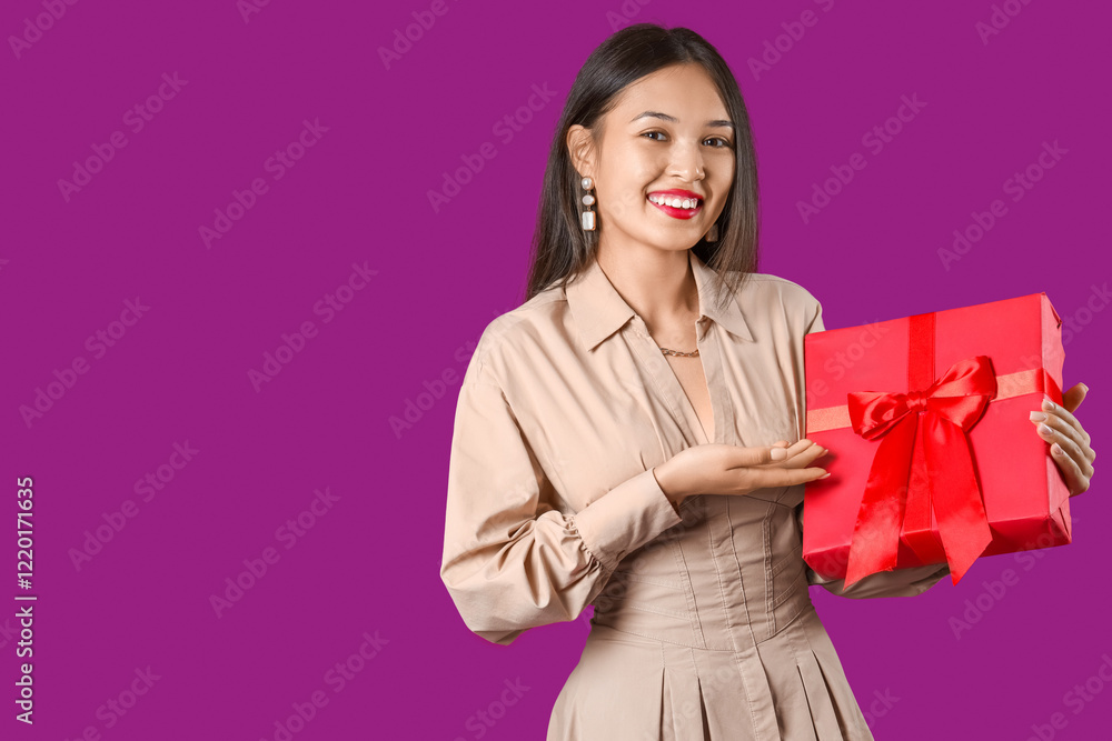 Beautiful young Asian woman pointing at gift box on purple background Beautiful young Asian woman pointing at gift box on purple background