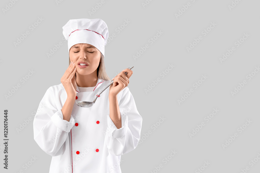 Young female chef with ladle suffering from tooth ache on grey background Young female chef with ladle suffering from tooth ache on grey background