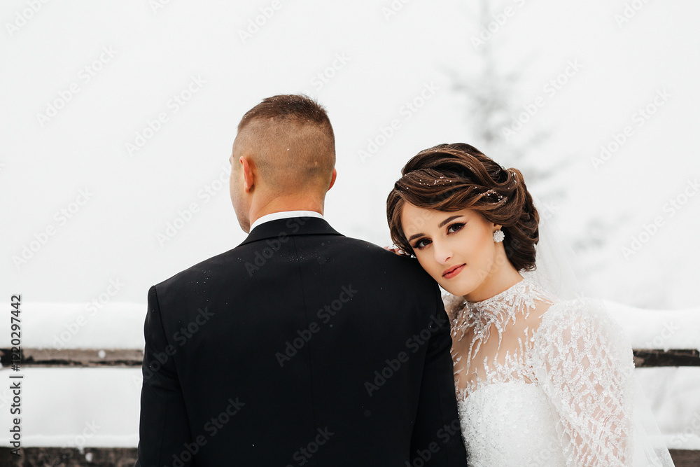 couple against the backdrop of a snowy landscape. The man is wearing a black suit with a white shirt and a black tie. He is holding a bouquet of white flowers in his hands. couple against the backdrop of a snowy landscape. The man is wearing a black suit with a white shirt and a black tie. He is holding a bouquet of white flowers in his hands.