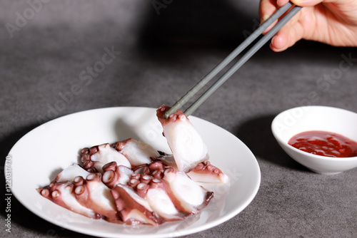 Pick up an octopus on a white plate with chopsticks. Fresh seafood dishes and red chili-pepper paste.
 photo