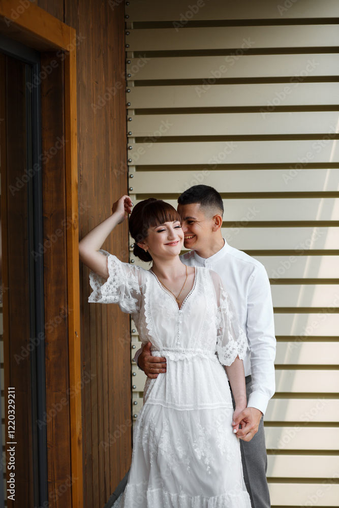 the bride and groom stand against the background of a light wall with horizontal stripes. The woman has closed her eyes and looks relaxed, and the man is smiling. the bride and groom stand against the background of a light wall with horizontal stripes. The woman has closed her eyes and looks relaxed, and the man is smiling.