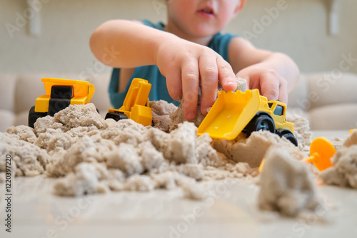 The toddler baby has fun playing a construction game with kinetic sand and plastic tools. Kid aged three year