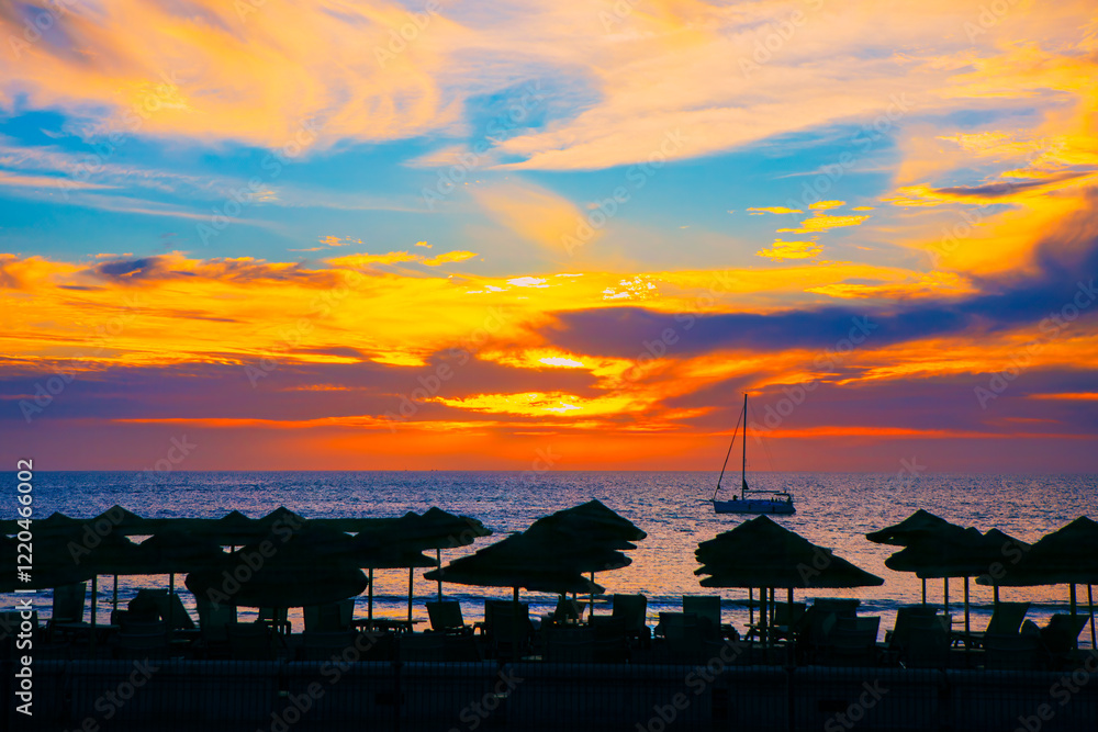 Golden hour hues paint the sky, casting a tranquil glow over the ocean. Silhouettes of beach umbrellas stand guard against the fading light. Serene beach scene at sunset with a vibrant sky