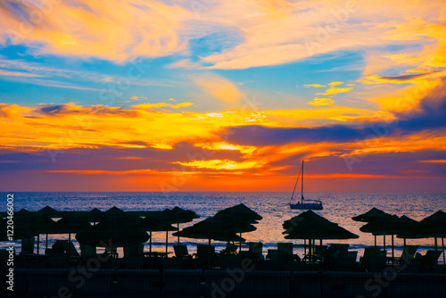 Obraz na płótnie Golden hour hues paint the sky, casting a tranquil glow over the ocean. Silhouettes of beach umbrellas stand guard against the fading light. Serene beach scene at sunset with a vibrant sky w salonie