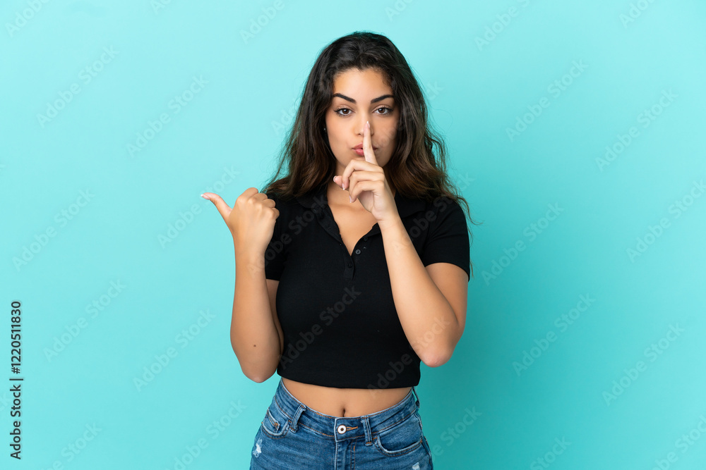 Young caucasian woman isolated on blue background pointing to the side and doing silence gesture Young caucasian woman isolated on blue background pointing to the side and doing silence gesture