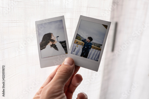 Canvas Print A father's hand holds two analog instant camera paper photographs of his childre