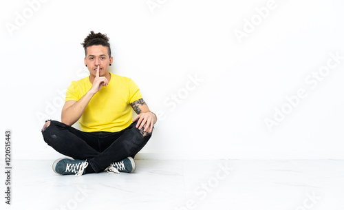 Caucasian man sitting on the floor showing a sign of silence gesture putting finger in mouth photo