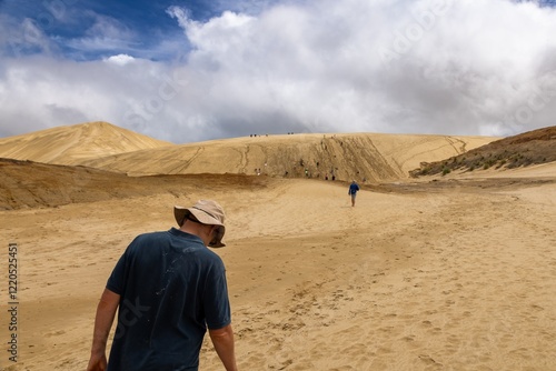 Hikers ascend a large sand dune. Cloudy day. Tourist activity. TE PAKI DUNES, NORTHLAND, NZ photo