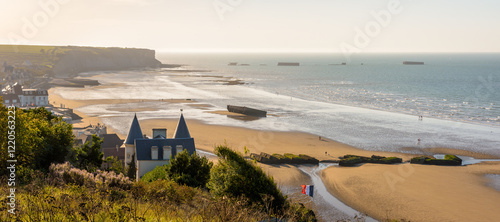 Panoramic view over Arromanches beach and Cap Manvieux in Normandy, France, at sunset with remains of the WWII artificial Mulberry harbour lying on the sand and in the sea.