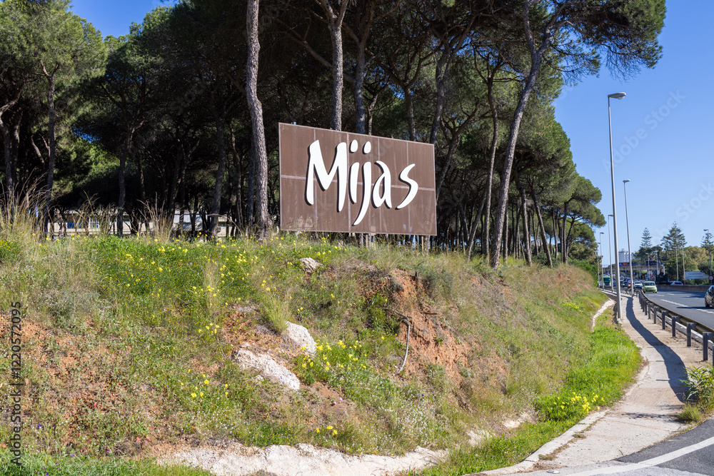 Photo of the street sigh of Mijas which is a town in the southern area of Spain in the summer time by the side of a busy motorway road road showing the sign by trees