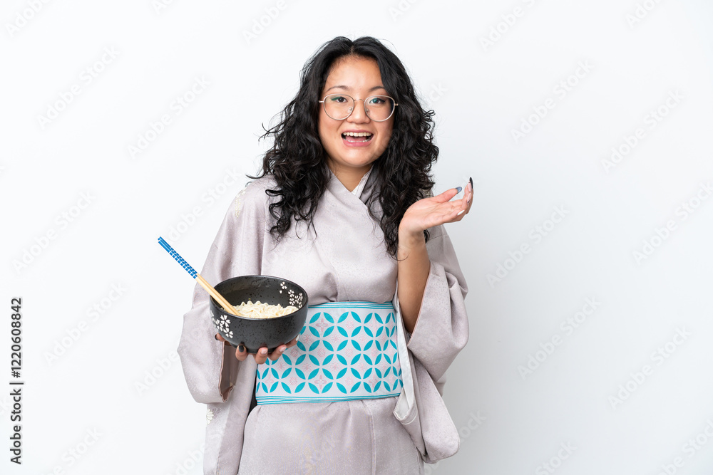 Young asian woman wearing kimono isolated on white background with shocked facial expression while holding a bowl of noodles with chopsticks Young asian woman wearing kimono isolated on white background with shocked facial expression while holding a bowl of noodles with chopsticks