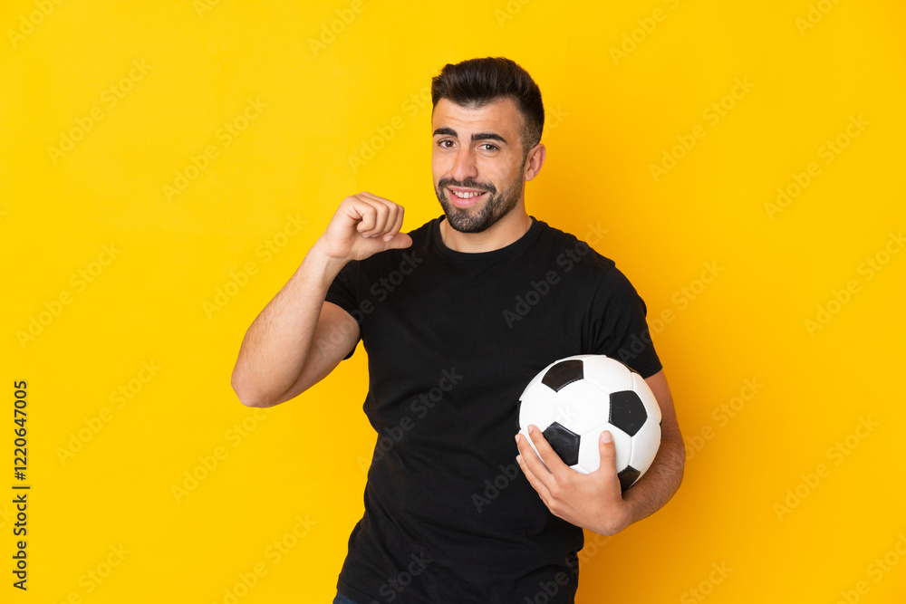 Caucasian man over isolated yellow background with soccer ball and proud of himself Caucasian man over isolated yellow background with soccer ball and proud of himself