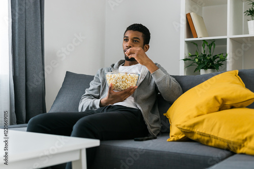 Cheerful curly haired ethnic african american male in casual clothes resting at home on comfortable sofa while watching tv channels or movie during weekend. Tv set, online television and entertiment photo