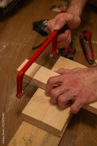 A person is sawing a wooden block with a red-handled hacksaw on a wooden surface photo