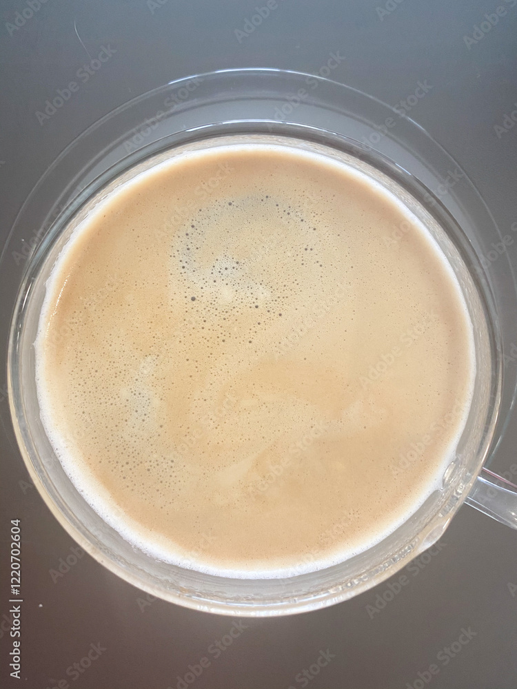 Top view of a frothy coffee in a transparent glass cup placed on a dark surface. Top view of a frothy coffee in a transparent glass cup placed on a dark surface.